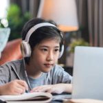 Asaian child Boy kid  taking an E-learning learning online class from school teacher by digital remote device laptop internet meeting in living room ,asia teen wear headphone using laptop e learning class at home