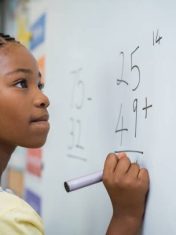 Portrait of african girl writing solution of sums on white board at school. Black schoolgirl solving addition sum on white board with marker pen. School child thinking while doing mathematics problem.